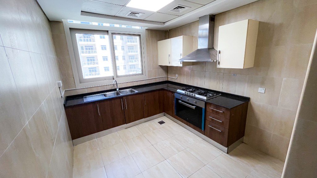 Fitted kitchen with dark wood cabinets and a gas hob in Azizi Freesia