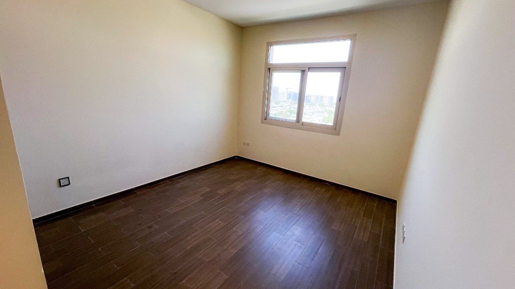 Empty bedroom with dark wood floors and a window in Azizi Freesia